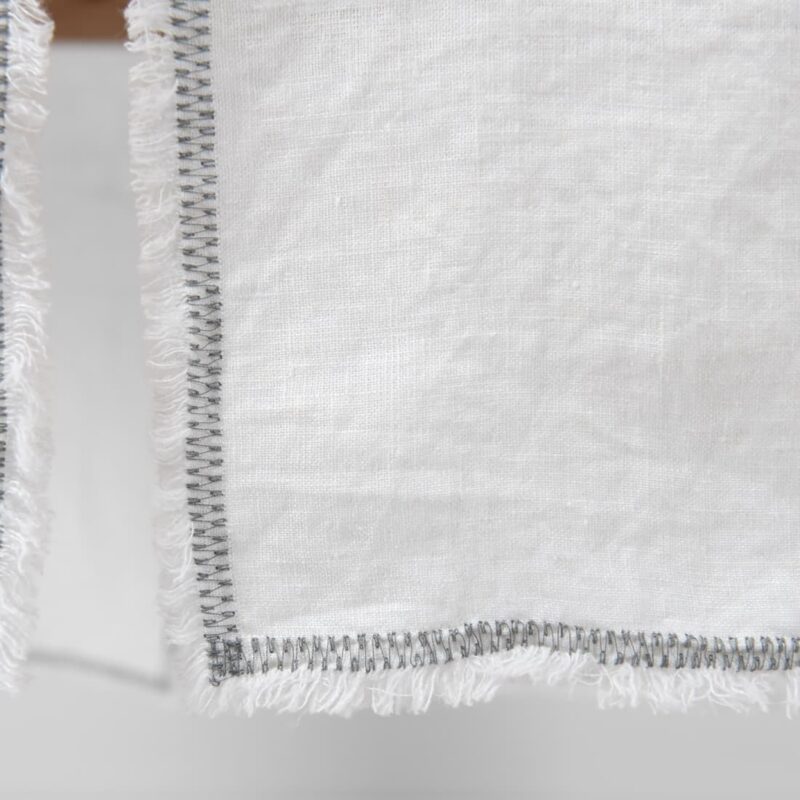 white linen runner with decorative stitch with loose fringes.