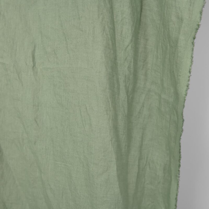 Washed linen fabric in muted light green, fabric edge